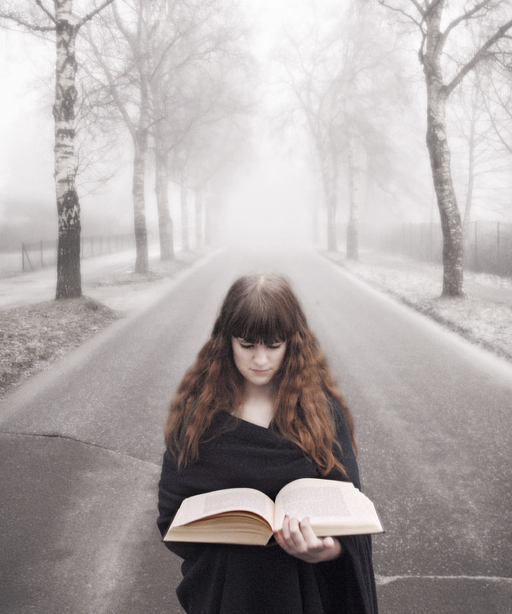 woman in black dress reading book on road during daytime
