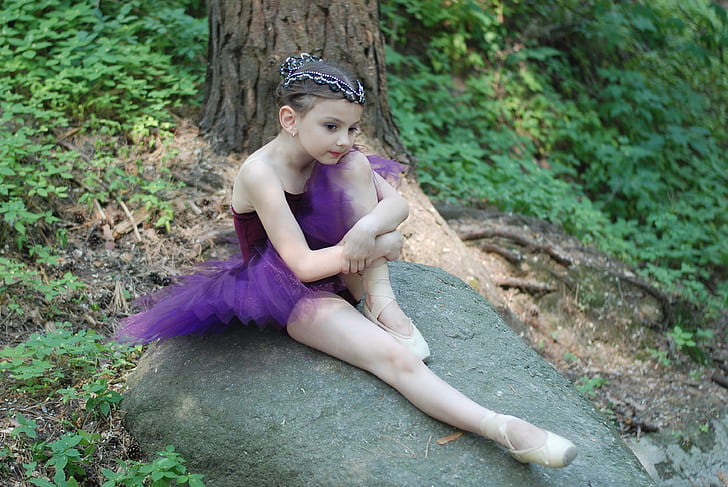 girl wearing purple tutu ballerina dress sits on gray rock