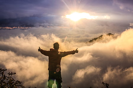 man standing on mountain cliff facing clouds
