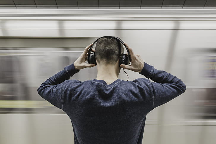 man wearing gray sweatshirt holding headphones in front on train station