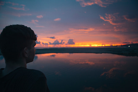 man wearing black top near body of water during sunset