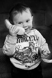 grayscale photo of toddler wearing jacket holding telephone