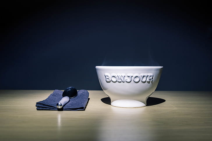 Bonjour Embossed White Ceramic Bowl on Table Beside Stainless Steel Spoon on Black Table Textile