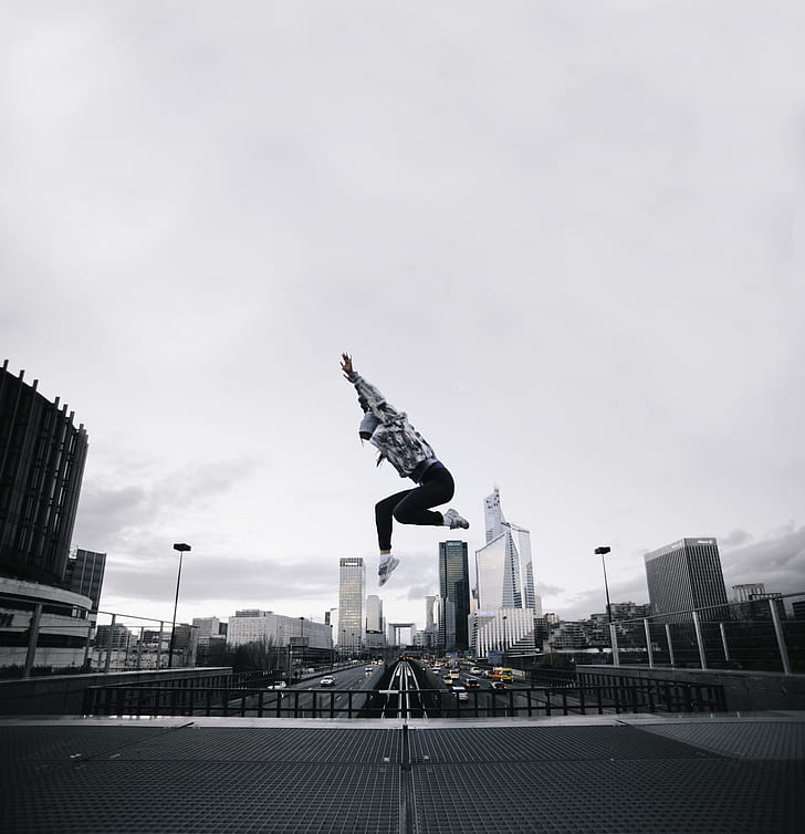 person wearing hoodie jumping on building photography