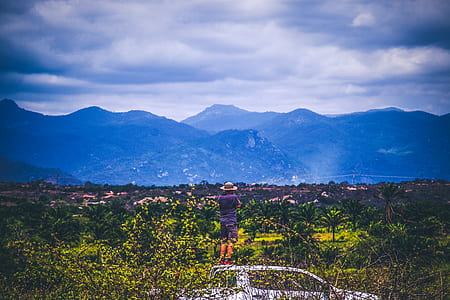 Person Wearing Sun Hat Looking At Mountains Under Cloudy Sky