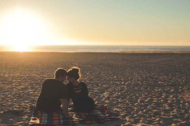 man and woman looking at each other on beach during sunset