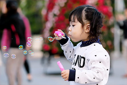 Toddler Girl Wearing White and Black Sweater Holding Plastic Bottle of Bubbles at Daytime
