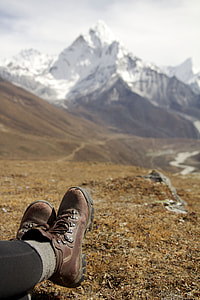 depth of field photography of person wearing brown leather hiking boots in front of mountains during daylight