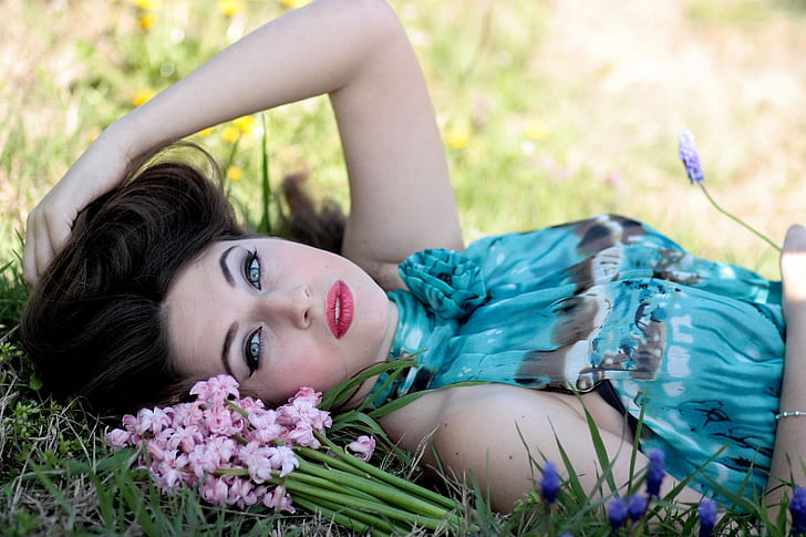 woman wearing blue sleeveless dress lying down on grass beside flowers