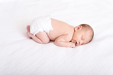 baby in white disposable diaper sleeping on white cushion