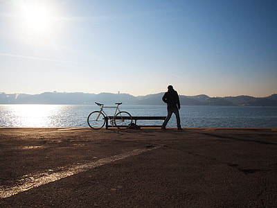silhouette of man beside white fixie bike watching ocean water view during daytime