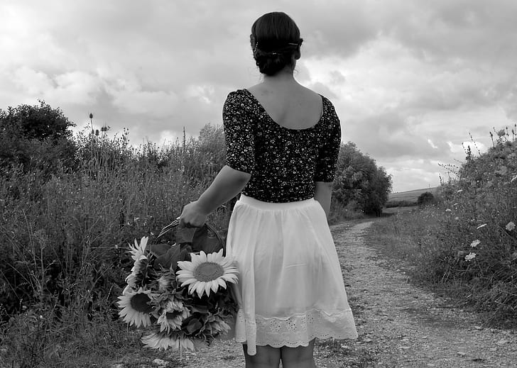 greyscale photography of woman holding basket with sunflower