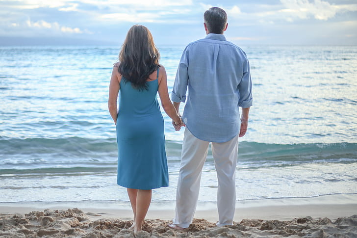 man and woman standing on shoreline while holding hands