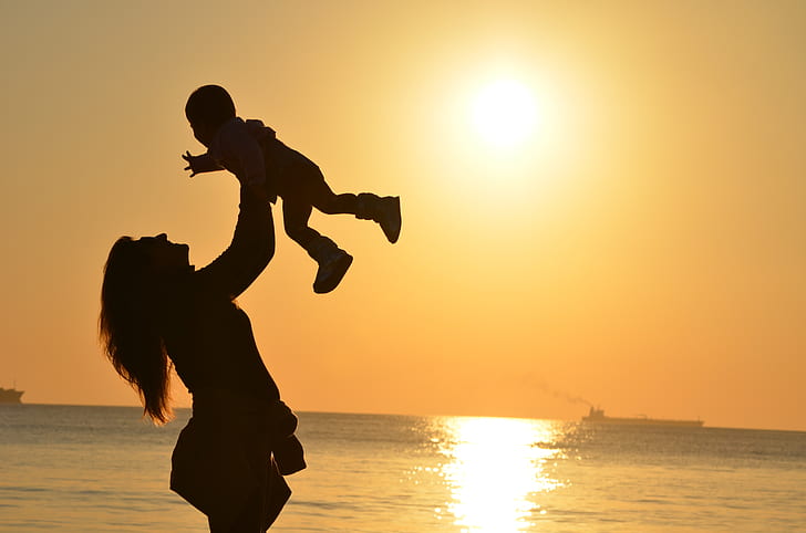 silhouette lifting her baby upward near sea during sun set