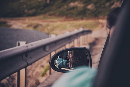 woman wears green jacket inside car seen on vehicle left mirror