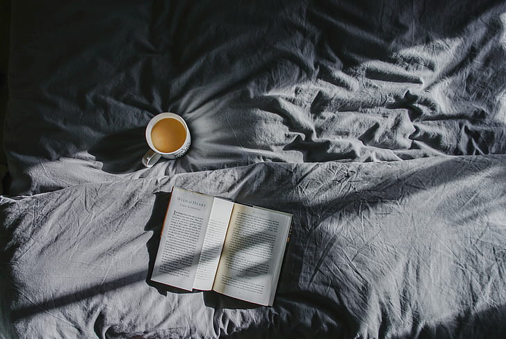 open book near mug on bed cover