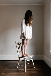 woman in white long-sleeved dress standing on white wooden chair near corner of the room