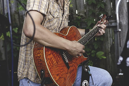 man in brown, black, and white plaid button-up t-shirt using brown acoustic guitar