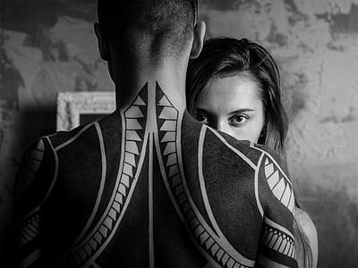 grayscale photography of woman hiding front of man with back tattoo