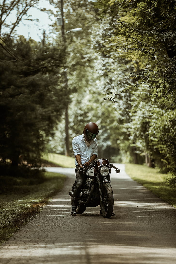 man wearing full-face helmet while riding motorcycle on asphalt roadway between trees during daytime