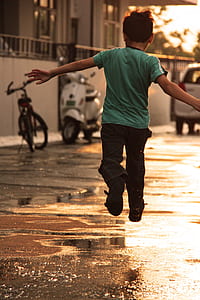 boy in teal t-shirt and black pants jumping on road