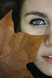 closeup photo of person face with brown maple leaf