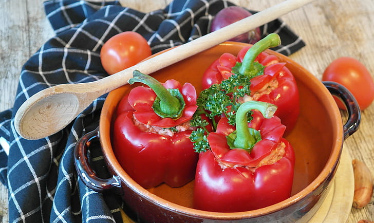 three red bell peppers in bowl with wooden spoon on table