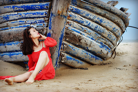woman wearing red cold-shoulder dress leaning on blue wooden boat