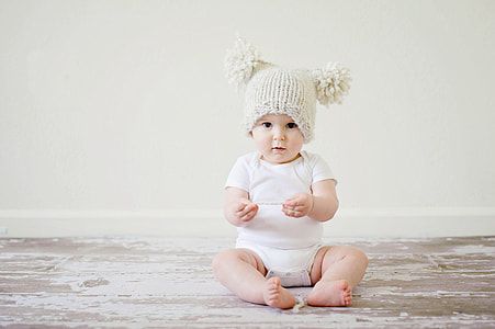 baby wearing white short-sleeved onesie and beige knit bobble hat