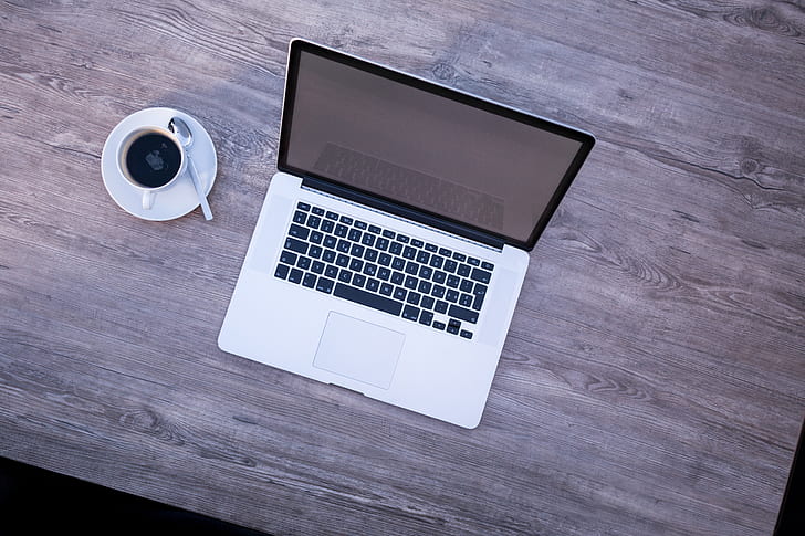 MacBook beside white coffee cup