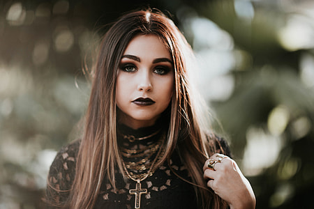 focus photography of woman with black lipstick wearing black lace top and cross pendant necklace during daytime
