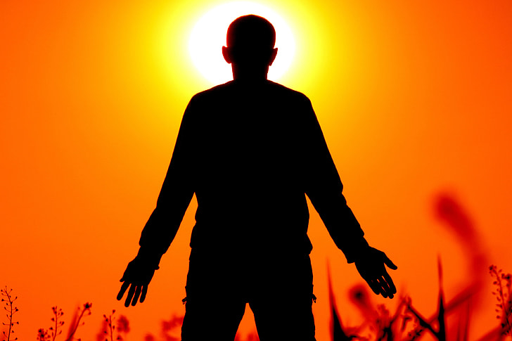 silhouette of person standing on grass field in front of orange sunset