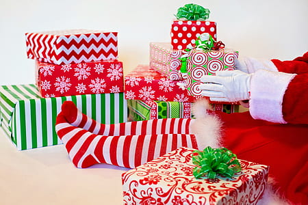 person wearing red and white santa dress sitting down near gifts holding green and red present