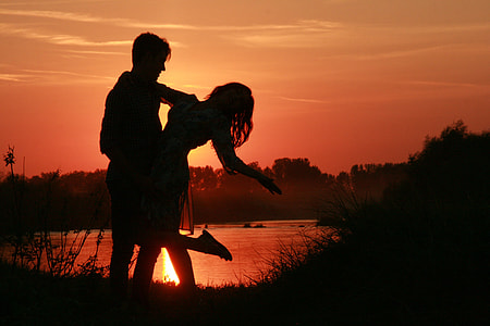 silhouette of man and woman near body of water during daytime