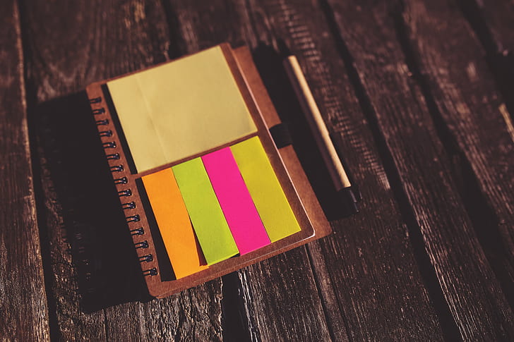 yellow, pink, and orange sticky notes on brown notebook