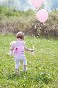 girl wearing pink sleeveless top with white pants holding balloons on green grass field