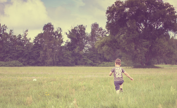 boy running on grass field near trees