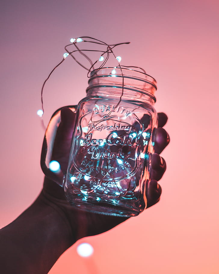 person holding clear glass mason jar with string light