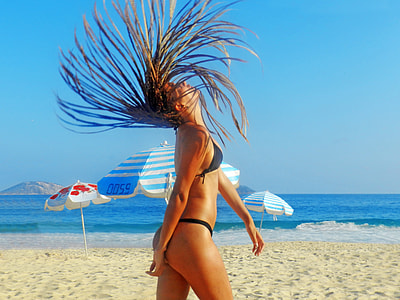 woman flips her hair on white sandy beach during daytime
