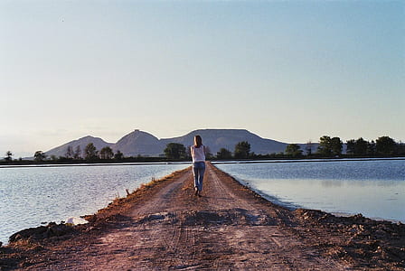 woman wearing blue jeans and white top near body of water at daytime