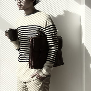 Standing Brunet Person Waring Eyeglasses and White Black Stripe Sweater Holding Mug and Briefcase