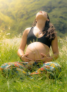 pregnant woman sitting on grassy field holding tummy