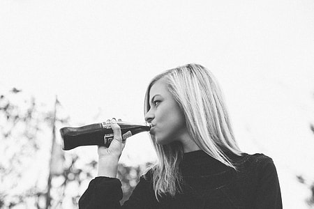 greyscale photography of woman in sweater drinking coca-cola in bottle during daytime