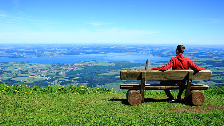 man in red hooded jacket sitting on brown wooden bench
