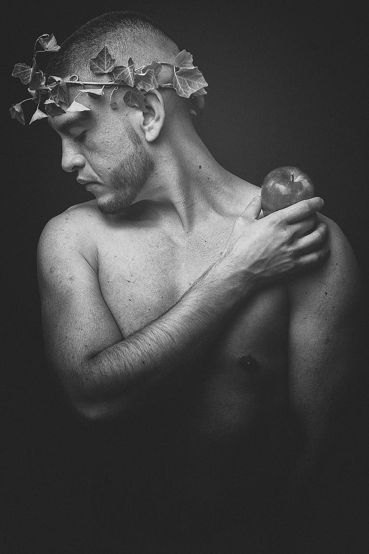greyscale photo of topless man wearing leaf headdress while holding apple