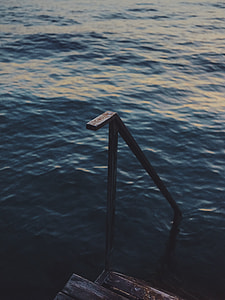 black metal railing with brown wooden stairs on body of water at daytime