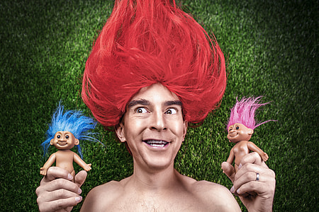person with red hair holding two troll toys