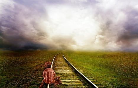 boy sitting on train rail under cloudy sky
