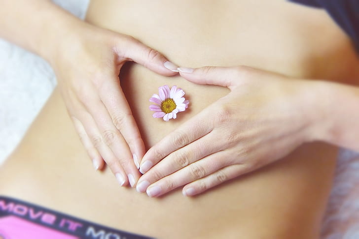 woman holding her stomach with pink and yellow marguerite daisy flower on navel in close-up photography