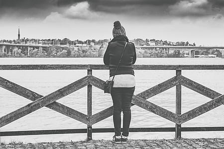 Woman Near Wooden Railing and Body of Water Grayscale Photo